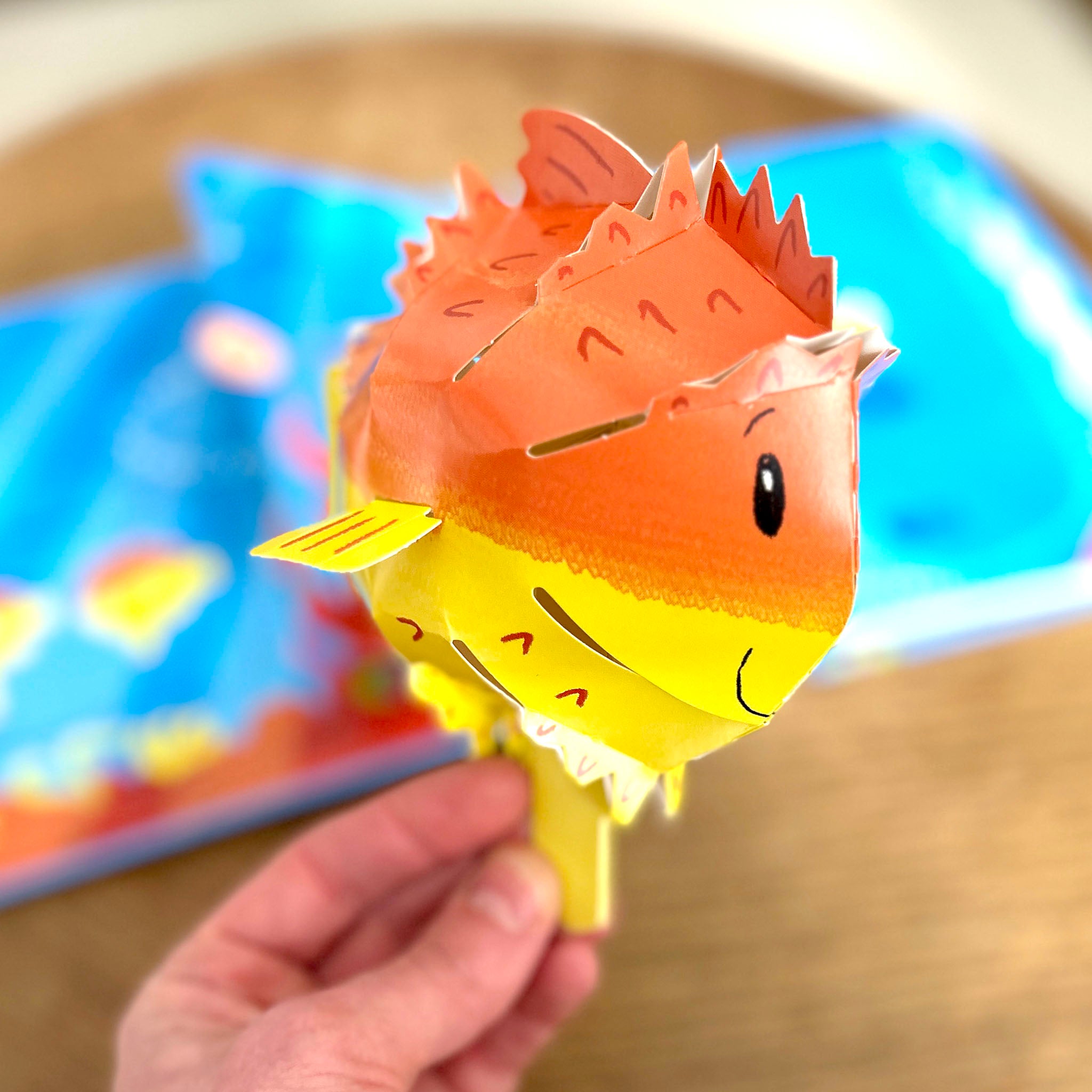 Hand holding a pop up paper pufferfish from Swim Along With Me